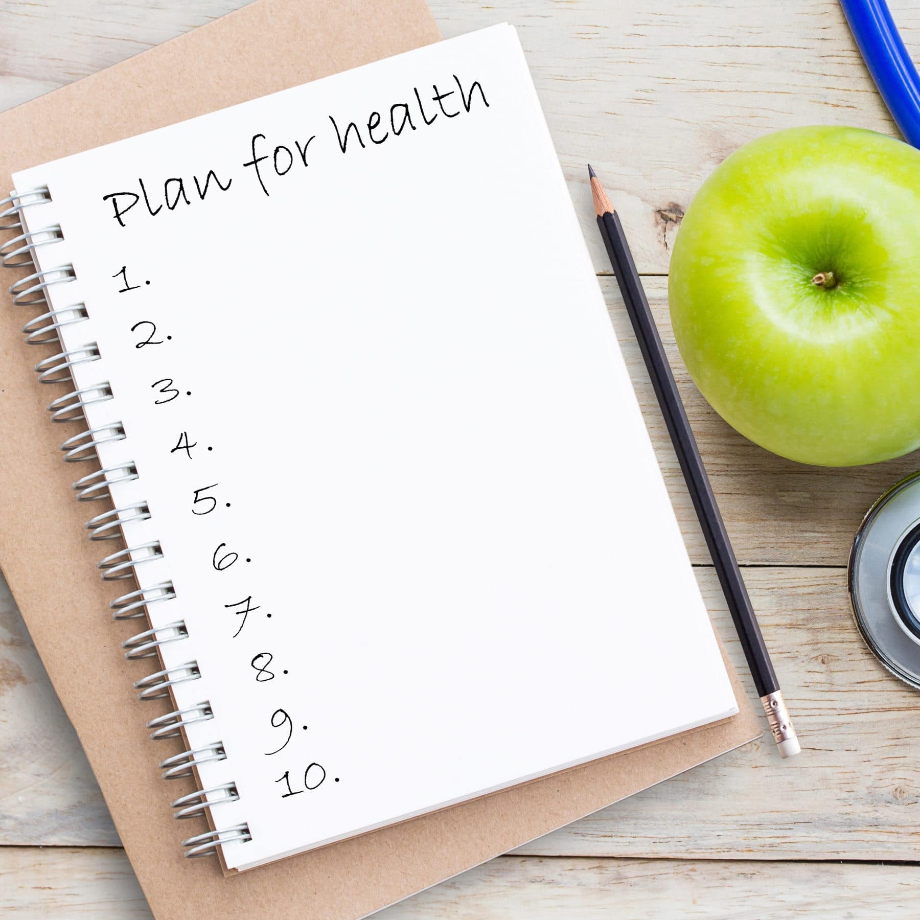 Top view blank notebook,pencil and green apple with blue stethoscope on wood table background.Concept for diet and healthcare, nutrition or medical insurance